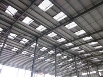 Interior view of a large warehouse ceiling with metal beams and natural ventilation systems.