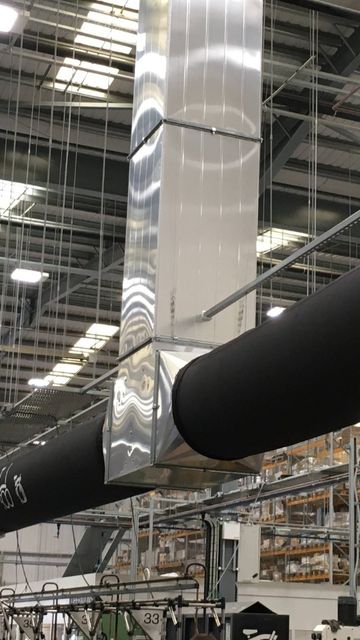Industrial warehouse interior with metal ductwork and overhead lighting, storage racks filled with boxes in the background.
