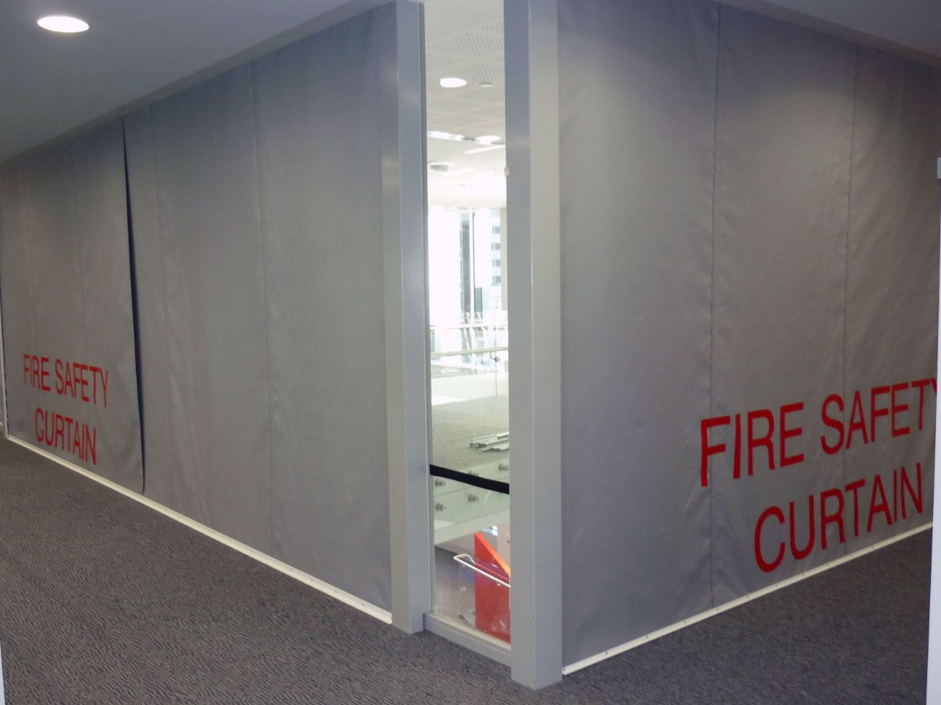 Gray Fire Curtain FM1 with red lettering cover walls in a hallway corner, ensuring protection and containment.