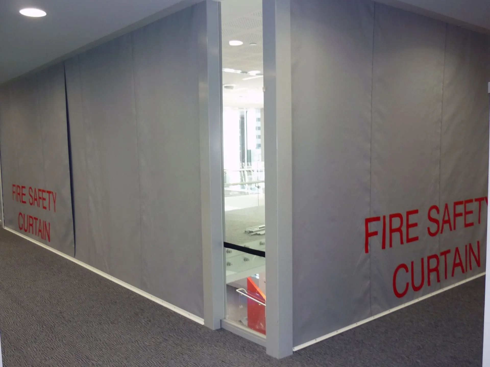 Gray Fire Curtain FM1 with red lettering cover walls in a hallway corner, ensuring protection and containment.