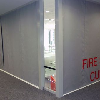 Gray Fire Curtain FM1 with red lettering cover walls in a hallway corner, ensuring protection and containment.