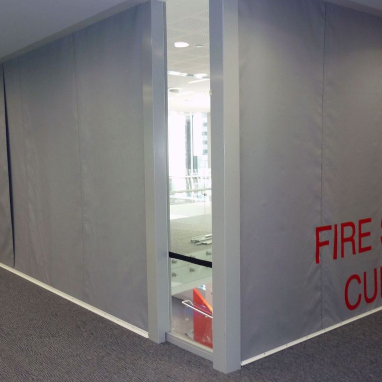 Gray Fire Curtain FM1 with red lettering cover walls in a hallway corner, ensuring protection and containment.
