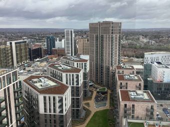 Aerial view of Canada Gardens with modern, high-rise buildings and urban landscape under a cloudy sky, with green spaces and roads visible in the distance.