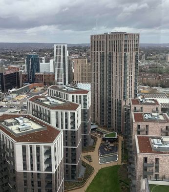 Aerial view of Canada Gardens with modern, high-rise buildings and urban landscape under a cloudy sky, with green spaces and roads visible in the distance.