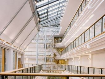 Modern, spacious atrium with a glass ceiling, large windows, and several floors visible. Ample natural light creates an open, airy atmosphere.