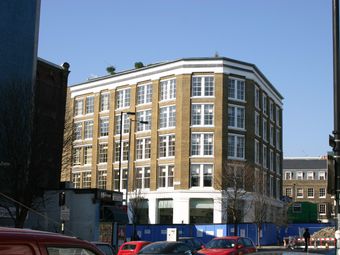 Colt Clerkenwell Hotel. A five-story brick building with large windows, corner location, clear blue sky, and parked cars on the street.