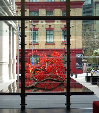 View through large glass windows of a modern lobby featuring a vibrant red art installation outside, contrasted against historic buildings.