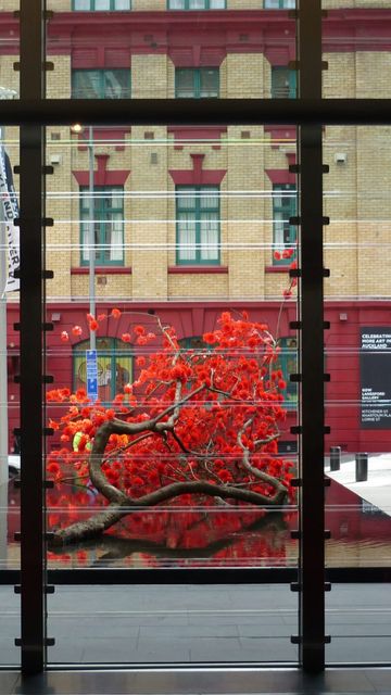 View through large glass windows of a modern lobby featuring a vibrant red art installation outside, contrasted against historic buildings.