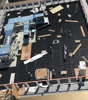 Rooftop view of a building with smoke ventilation systems, insulation, and scattered materials on a grid-like surface.
