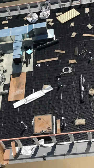 Rooftop view of a building with smoke ventilation systems, insulation, and scattered materials on a grid-like surface.