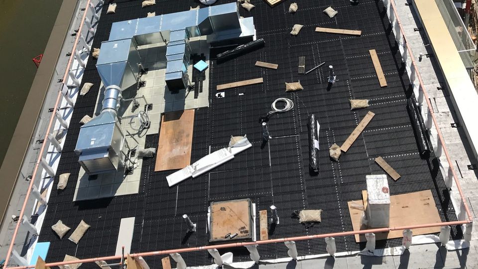 Rooftop view of a building with smoke ventilation systems, insulation, and scattered materials on a grid-like surface.