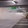 Two people in high-visibility vests operate a fog machine in a parking garage under a "Way out" sign.
