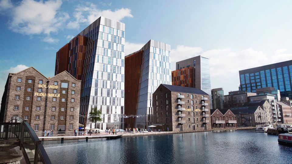 Modern glass buildings and historic brick warehouses along a waterfront, with boats docked in the foreground under a clear blue sky.