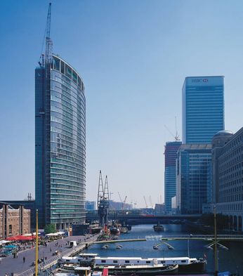 Skyline with modern skyscrapers and a historic building along a river, bustling with people and boats on a clear day.