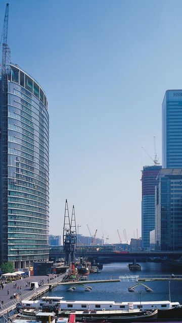 Skyline with modern skyscrapers and a historic building along a river, bustling with people and boats on a clear day.