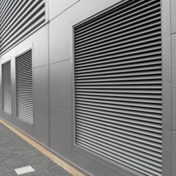 Metal-clad industrial building with large vented panels and parallel-lined corrugated texture, adjacent to a paved pathway.