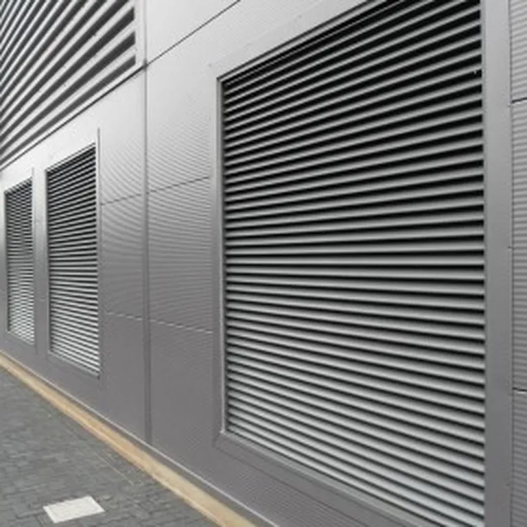 Metal-clad industrial building with large vented panels and parallel-lined corrugated texture, adjacent to a paved pathway.