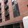 Red brick building facade with multiple windows and small balconies, viewed from a slightly angled perspective.