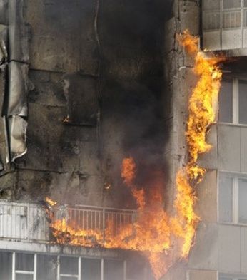 Flames engulf the side of a high-rise building, with smoke billowing from charred walls and damaged balconies.