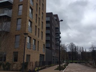Modern brick apartment buildings line a quiet street under a cloudy sky, with lampposts and bare trees.