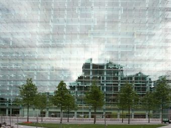 Civil Justice Centre in Manchester, a glass building facade with a grid pattern, showing the mirrored image of adjacent structures and a row of trees in front.