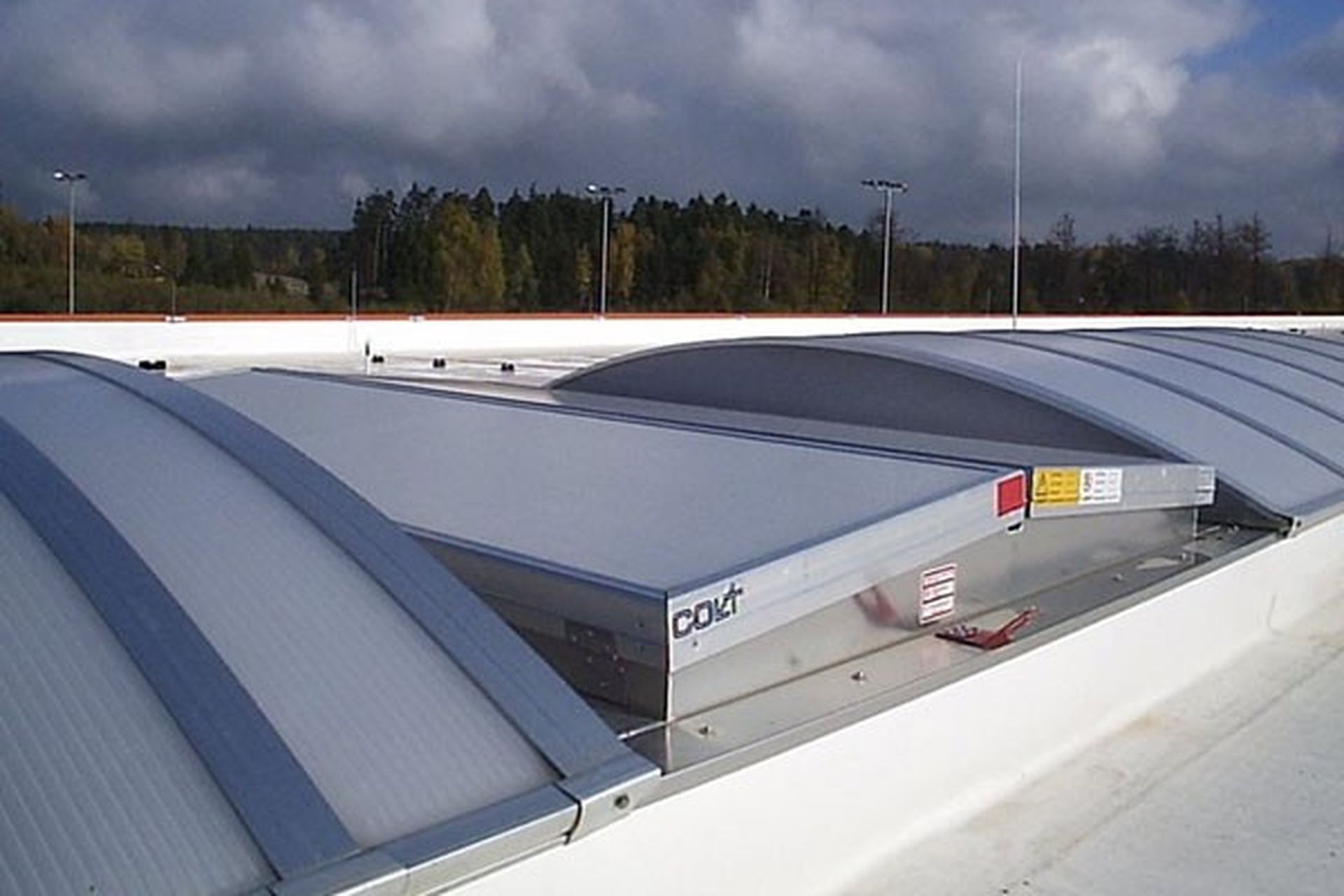 Curved metal roof ventilators under a cloudy sky, surrounded by trees in the distance, providing natural ventilation.
