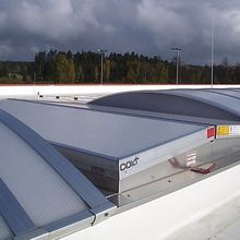 Curved metal roof ventilators under a cloudy sky, surrounded by trees in the distance, providing natural ventilation.