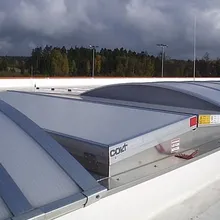 Curved metal roof ventilators under a cloudy sky, surrounded by trees in the distance, providing natural ventilation.