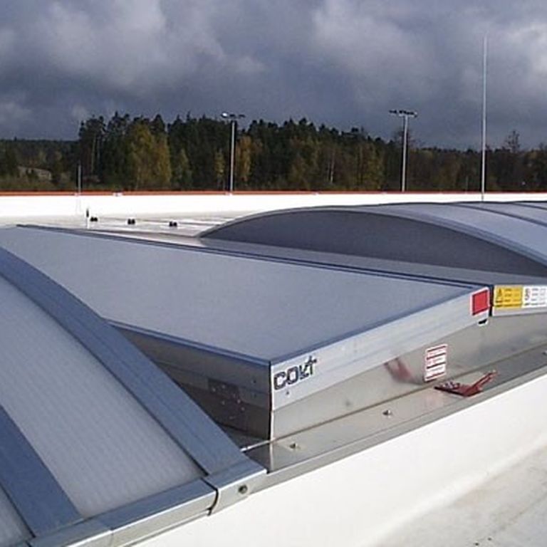 Curved metal roof ventilators under a cloudy sky, surrounded by trees in the distance, providing natural ventilation.