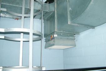 A metal ventilation duct system running along a light blue wall, with a ladder-like structure nearby.