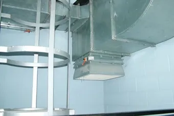 A metal ventilation duct system running along a light blue wall, with a ladder-like structure nearby.