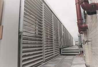 Rooftop view of large ventilation system with louvered panels beside red pipes.