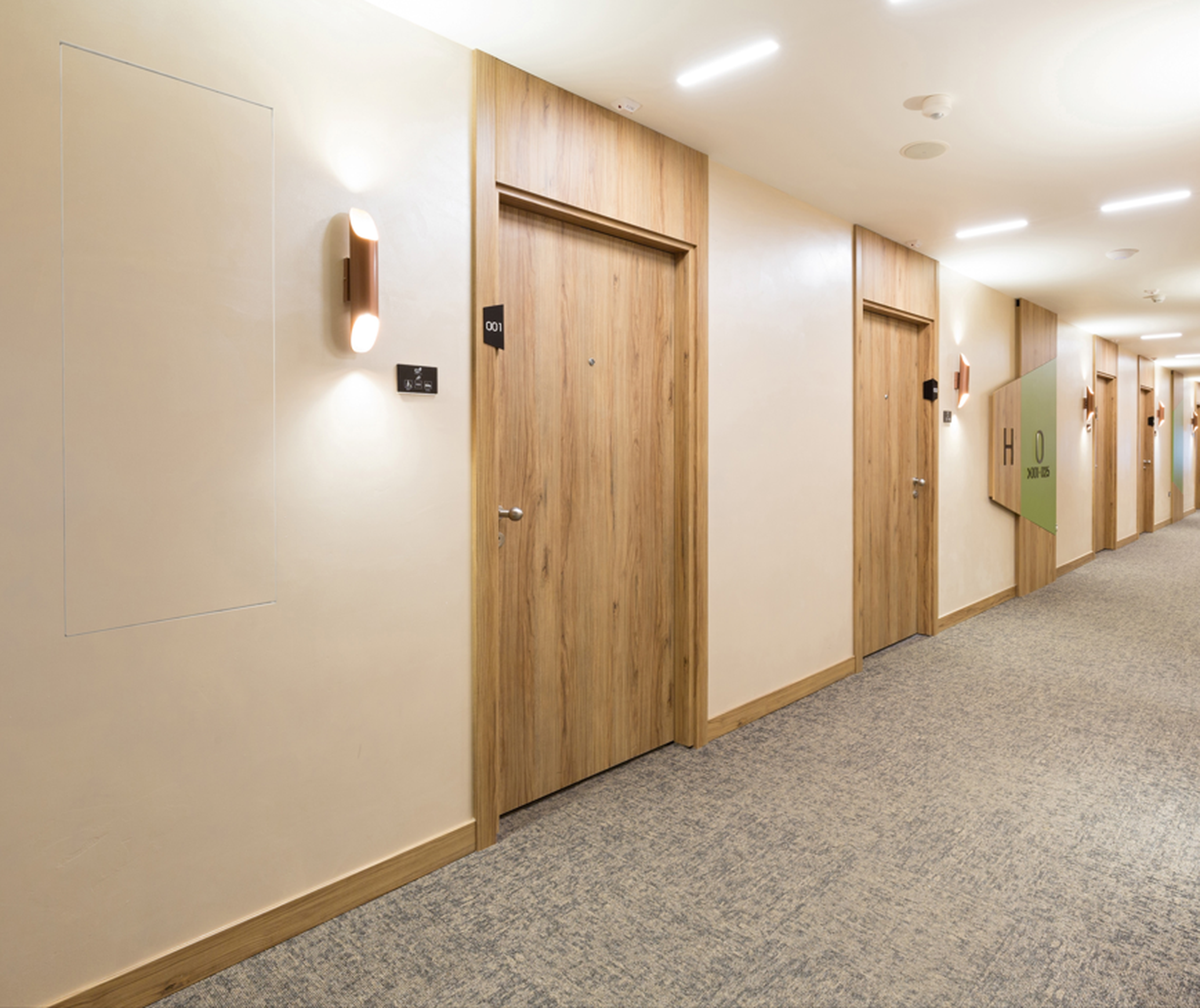 Hotel corridor with wooden doors, wall sconces, and carpeted flooring. Door labels include room numbers and signs.