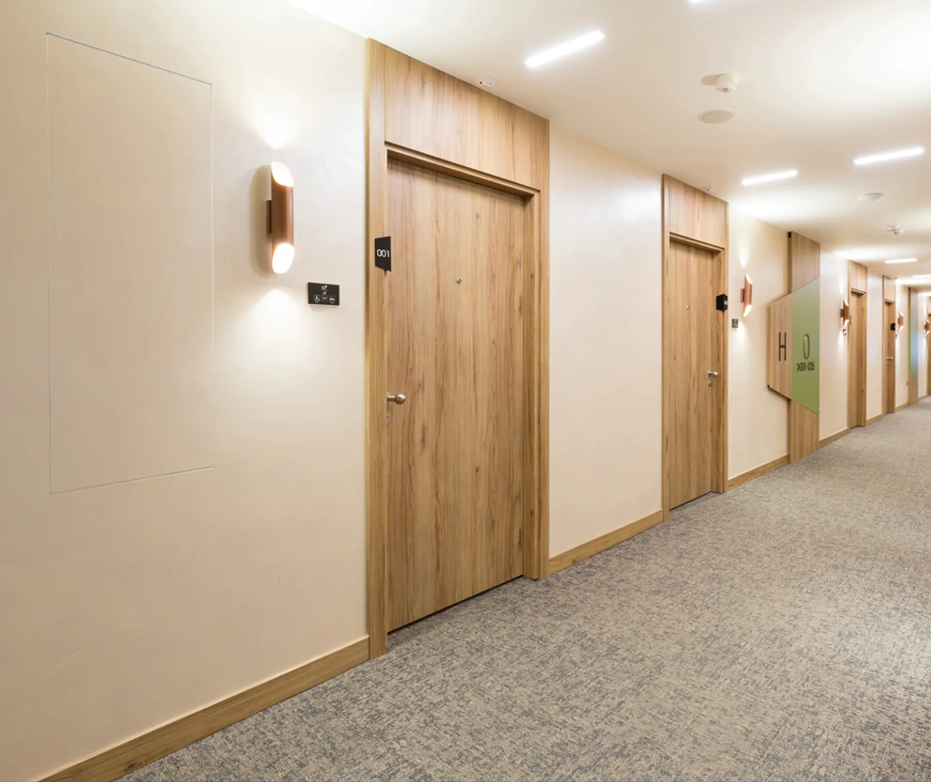 Hotel corridor with wooden doors, wall sconces, and carpeted flooring. Door labels include room numbers and signs.
