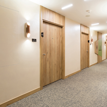 Hotel corridor with wooden doors, wall sconces, and carpeted flooring. Door labels include room numbers and signs.
