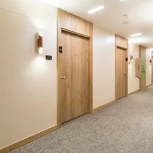 Hotel corridor with wooden doors, wall sconces, and carpeted flooring. Door labels include room numbers and signs.