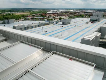 Rooftop view of a large, mostly empty parking structure with blue markings, surrounded by a suburban landscape under a cloudy sky.