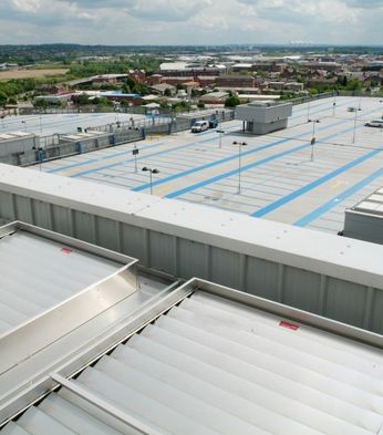 A large rooftop parking area over a shopping centre, overlooking an industrial and residential landscape under a cloudy sky.
