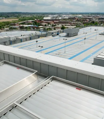 A large rooftop parking area over a shopping centre, overlooking an industrial and residential landscape under a cloudy sky.