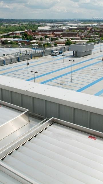 A large rooftop parking area over a shopping centre, overlooking an industrial and residential landscape under a cloudy sky.