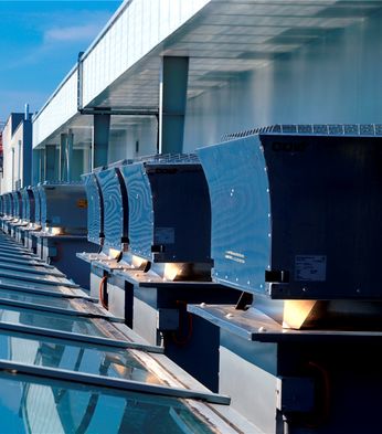 Row of roof mechanical ventilators, with a view of surrounding buildings and greenery in the distance.