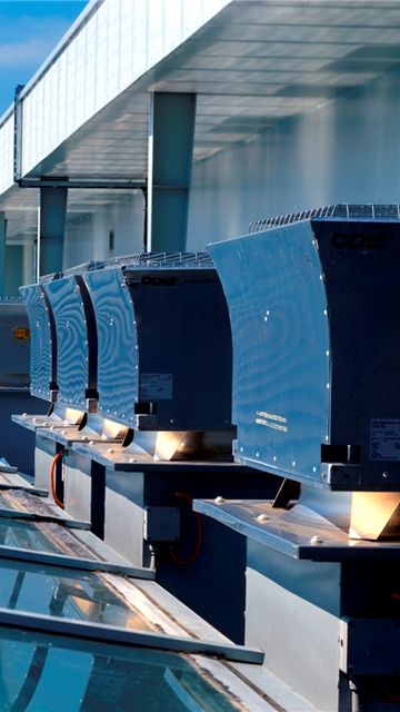 Row of roof mechanical ventilators, with a view of surrounding buildings and greenery in the distance.