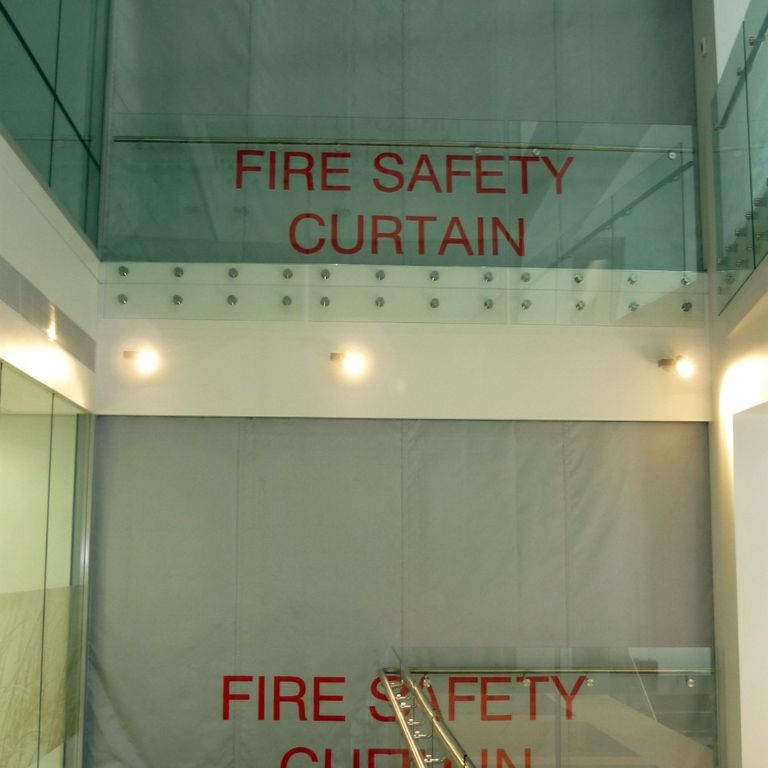 Stairwell with Fire Curtain FM1 deployed on two floors, featuring glass railings and beige walls.