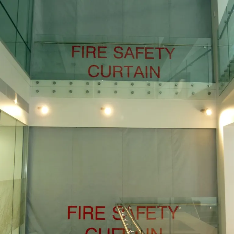Stairwell with Fire Curtain FM1 deployed on two floors, featuring glass railings and beige walls.