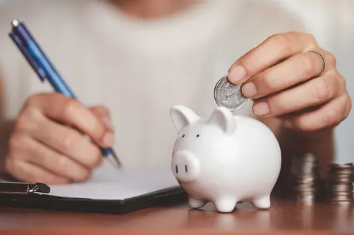 Sparschwein auf dem Tisch. Person mit Stift und Geld in der Hand, die Geld in das Schwein wirft