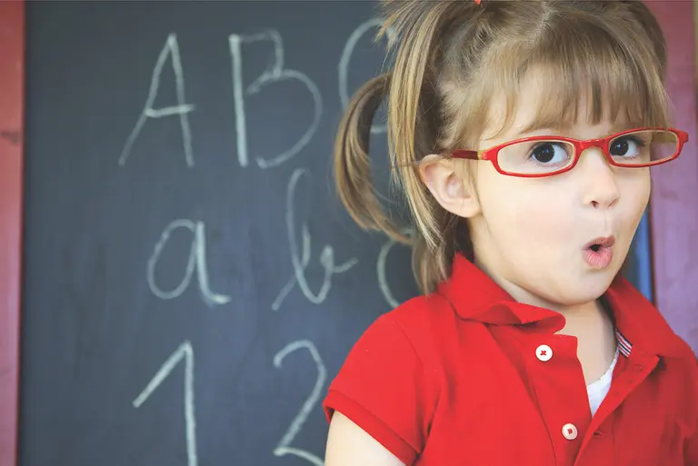 Schulmädchen mit Brille vor einer Tafel