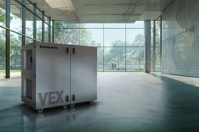 A large ventilation unit labeled "EXHAUSTO VEX" in a spacious, glass-walled room with trees visible outside.