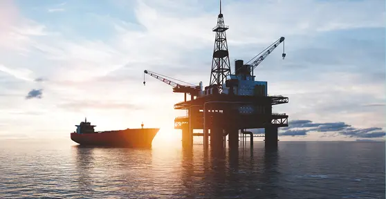 Plataforma de petróleo no mar ao lado de um navio-tanque, com o sol se pondo ao fundo.