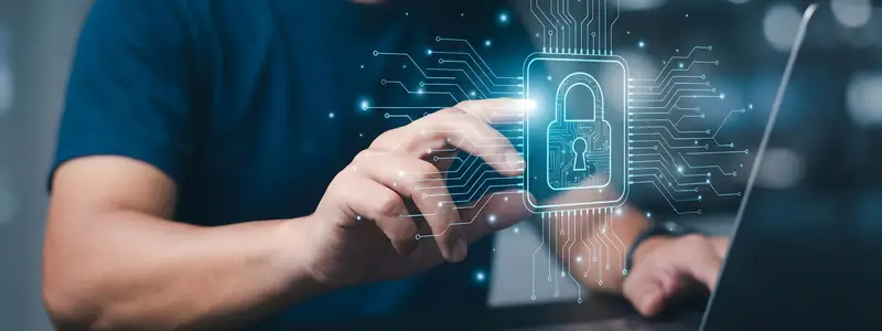 Homem de camiseta azul tocando em um ícone holográfico de cadeado conectado a circuitos digitais, ao lado de um laptop aberto.