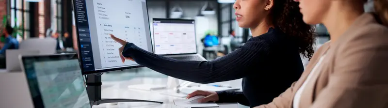 Mulher trabalhando em um laptop em um escritório iluminado, com gráficos e dashboards holográficos projetados à frente da tela.